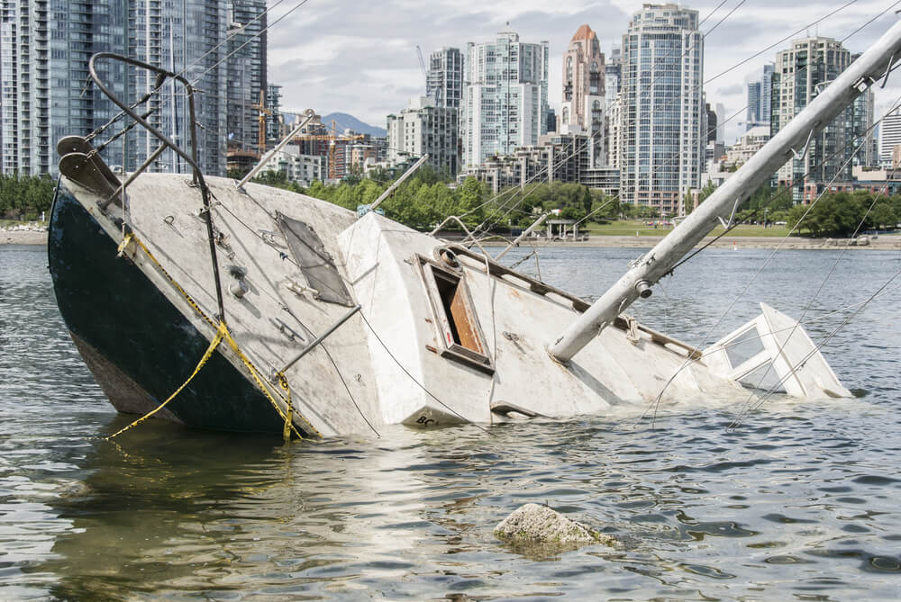 Sinking sailboat abandoned on the shore of a city.